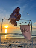 Rose gold balloons and a 'bliss' sign on a beach at sunset