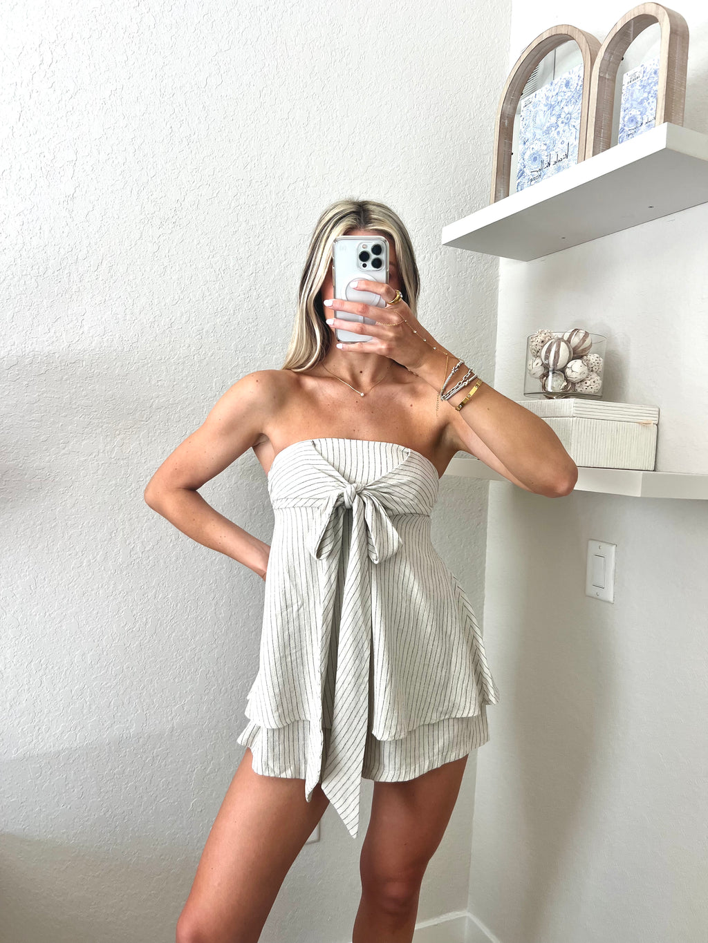 Woman taking a mirror selfie wearing an ivory with black pinstripes strapless romper.