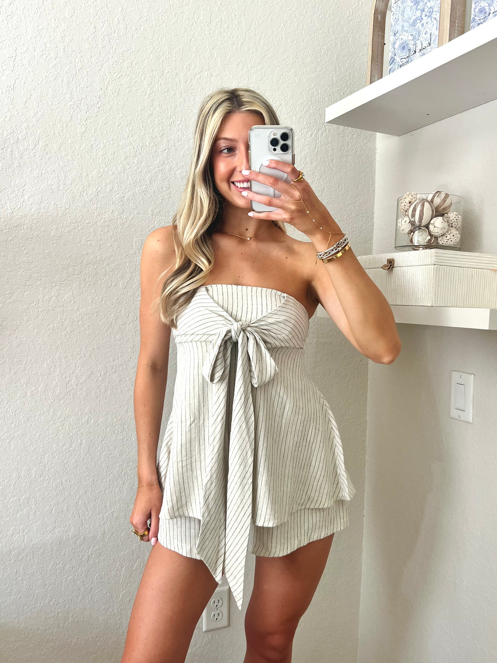 Woman taking a mirror selfie wearing an ivory with black pinstripes strapless romper.