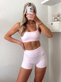 Woman taking a mirror selfie wearing a pink gingham, double layered sports bra and matching pink gingham biker shorts.