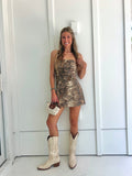 A woman wearing a strapless tiger printed dress and cream cowgirl boots with a cream purse standing against a white wall.