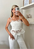 Woman taking a mirror selfie wearing a white lace top and white denim jeans.