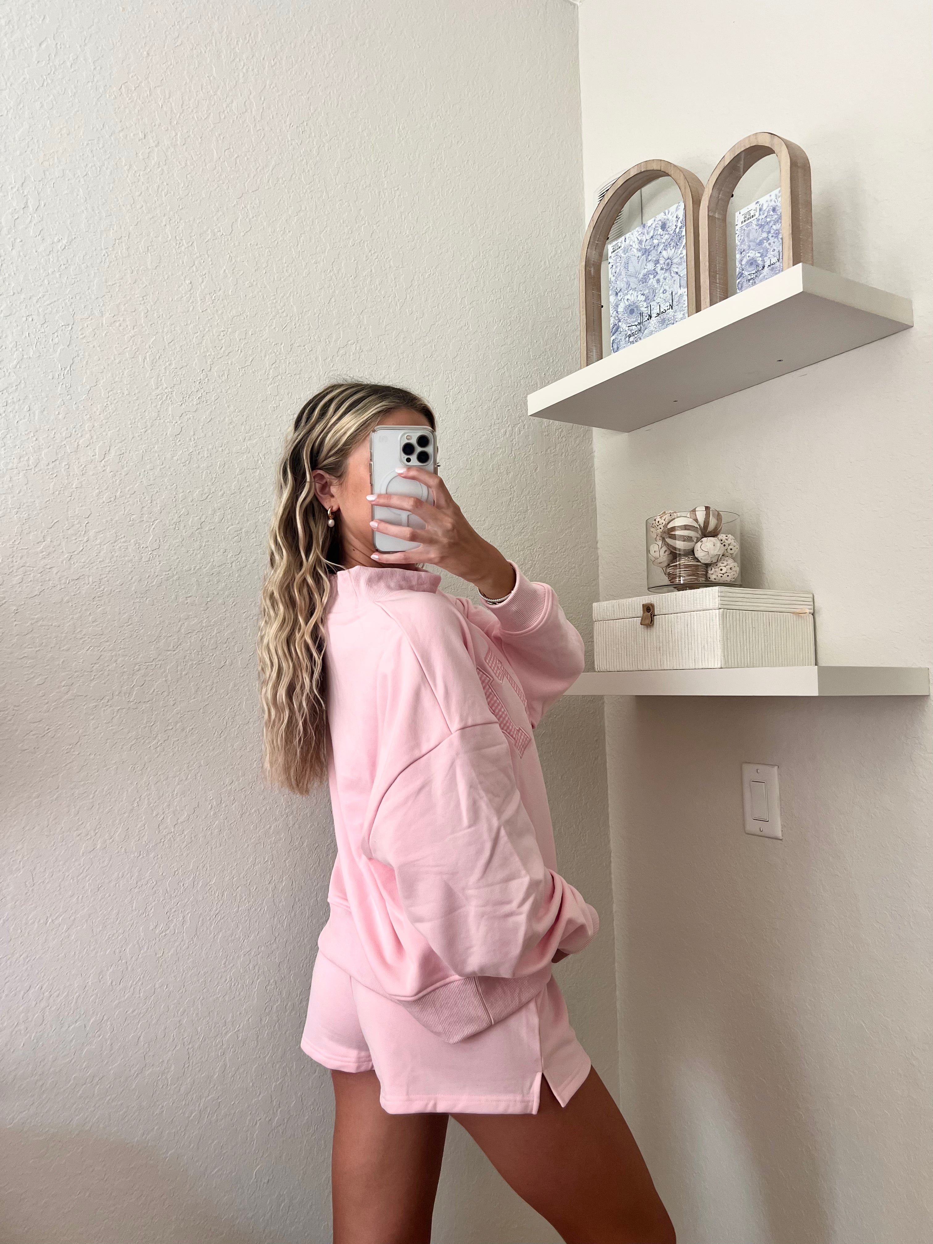 Woman wearing a pink sweatshirt with the word "Salty" on it and shorts set in a room with a shelf in the background.