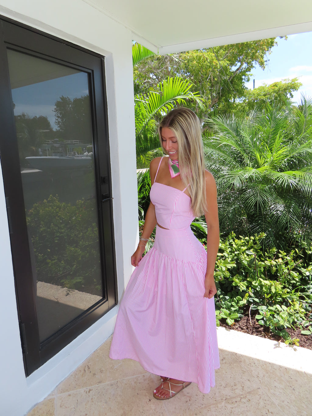 Woman in a pink and white striped maxi skirt set standing outdoors with greenery in the background