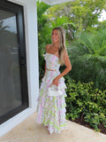 Woman holding a white purse in a patterned maxi skirt set standing near a glass door with greenery outside.