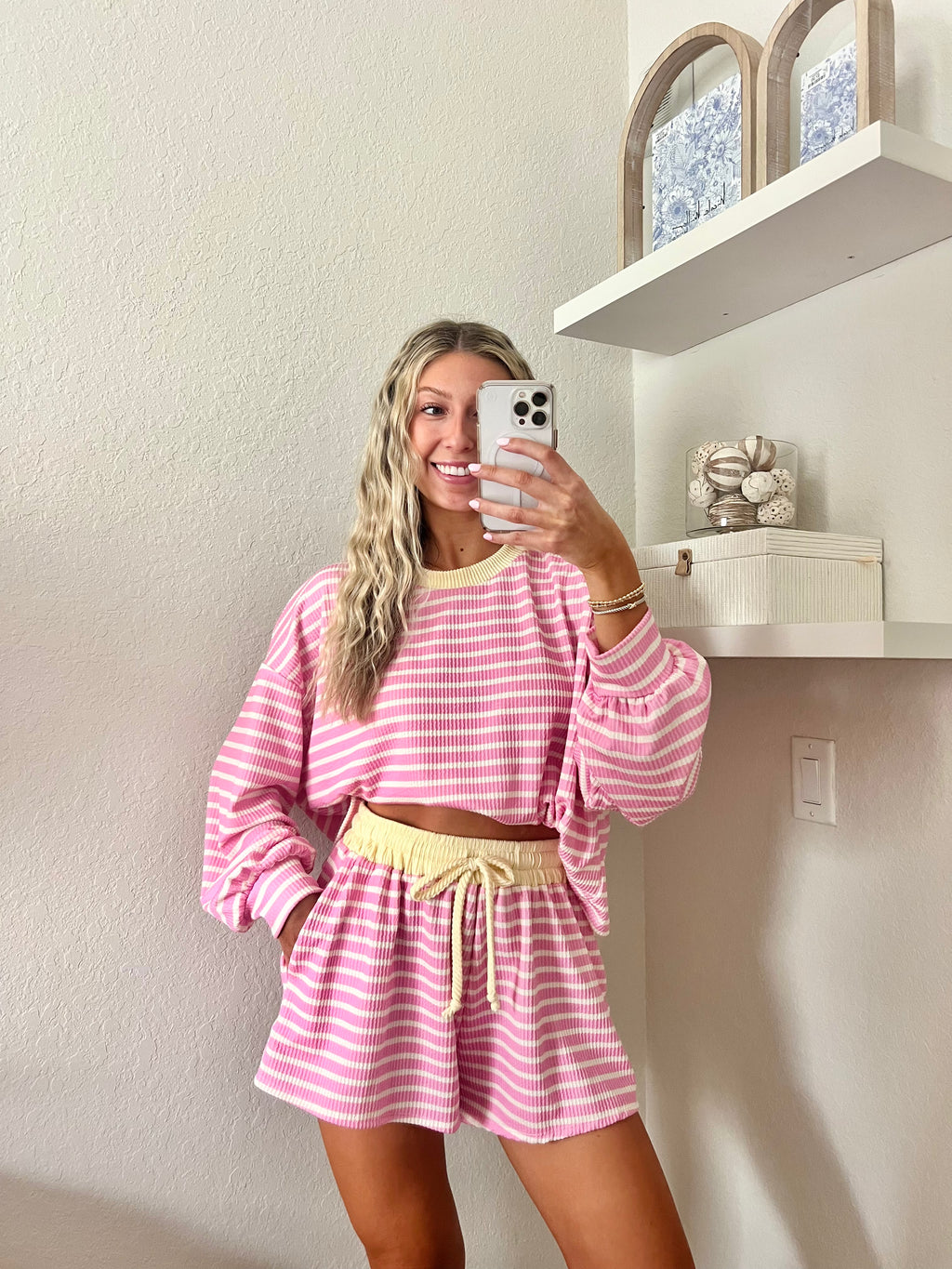 Woman wearing a pink and white striped long sleeve and shorts set with yellow trim taking a mirror selfie.