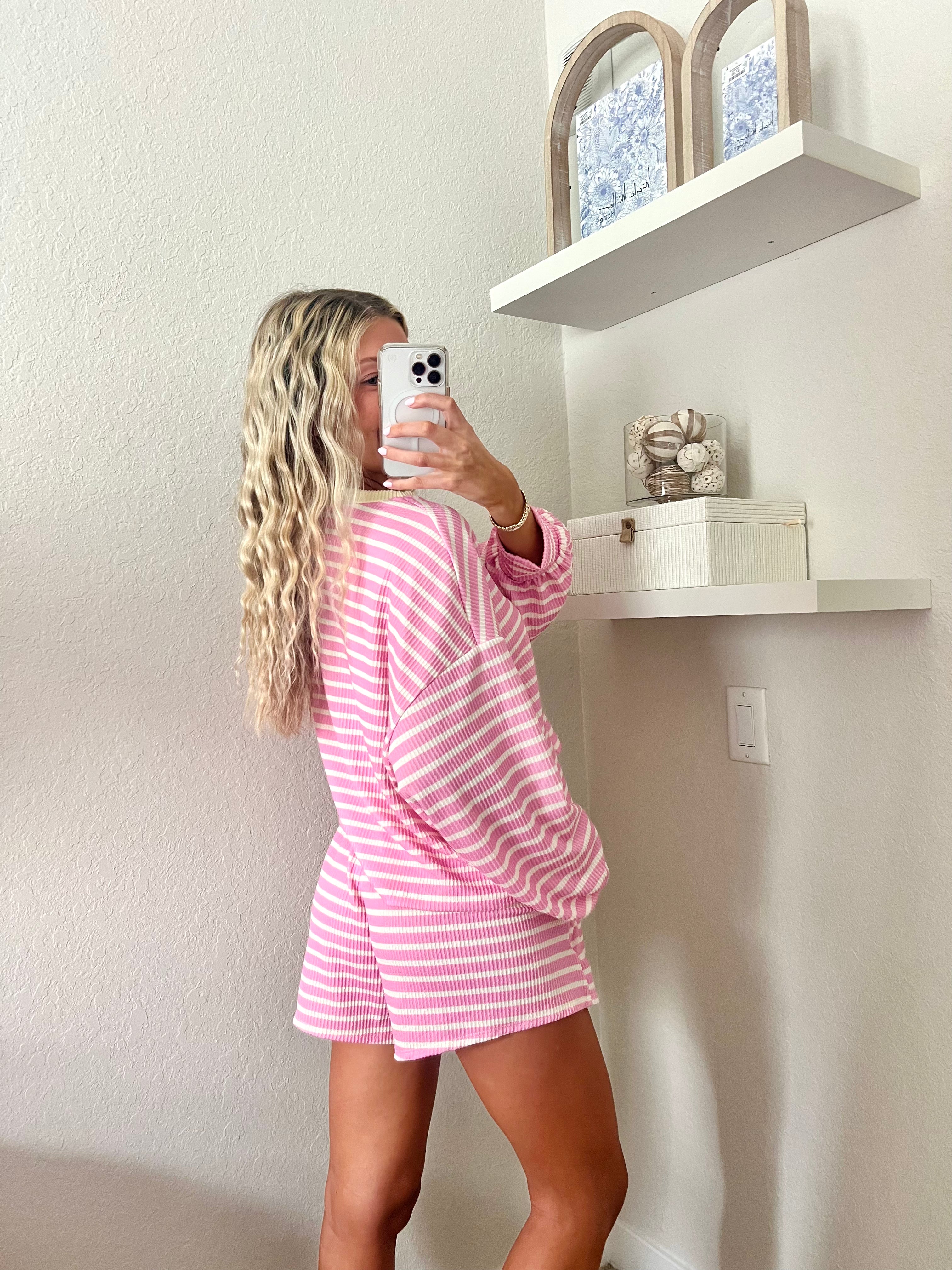 Woman wearing a pink and white striped long sleeve and shorts set with yellow trim taking a mirror selfie.