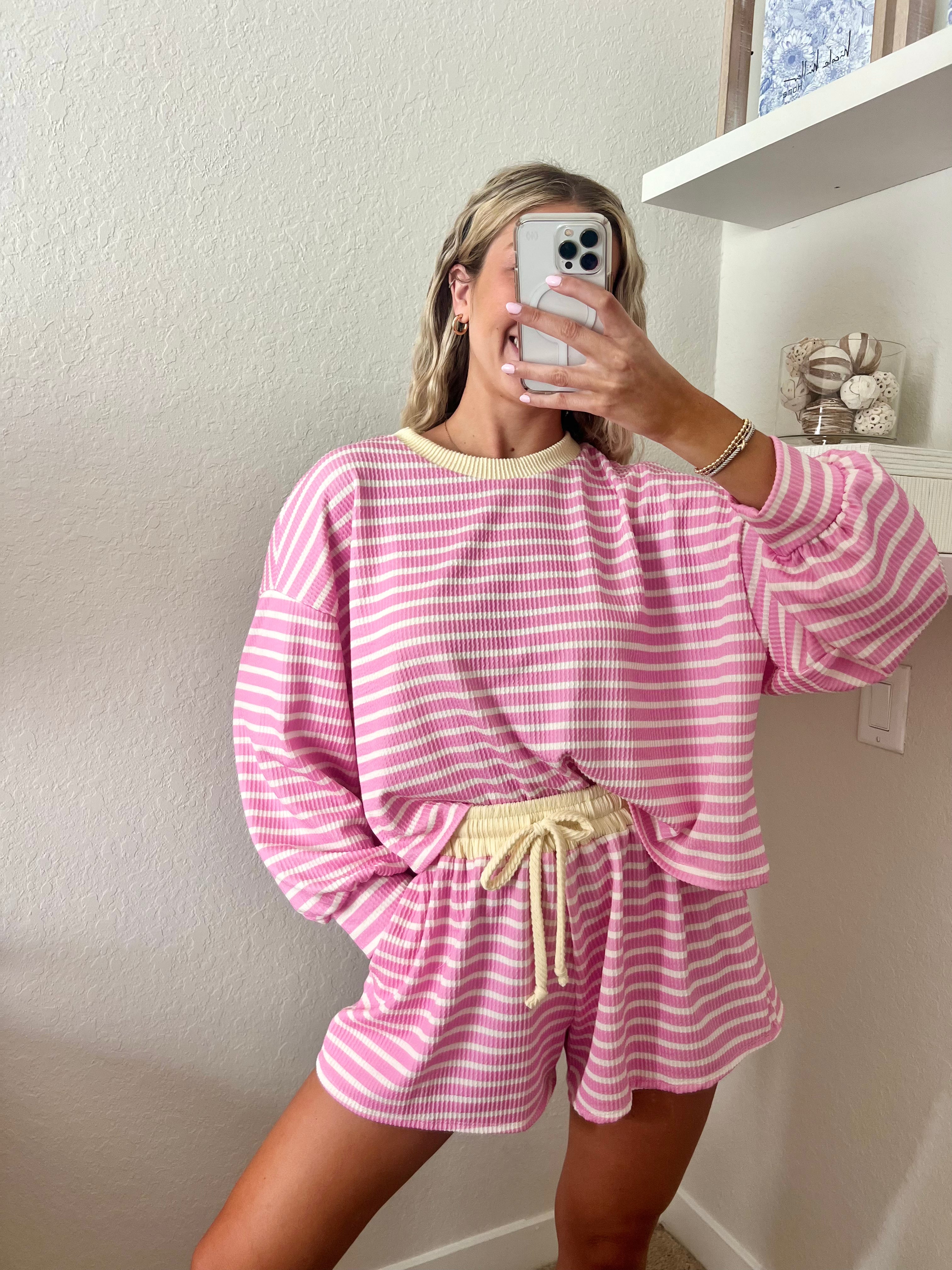 Woman wearing a pink and white striped long sleeve and shorts set with yellow trim taking a mirror selfie.