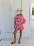 Woman wearing a red and white striped set that says "American girl" in navy, wearing a cowgirl hat and sandals.