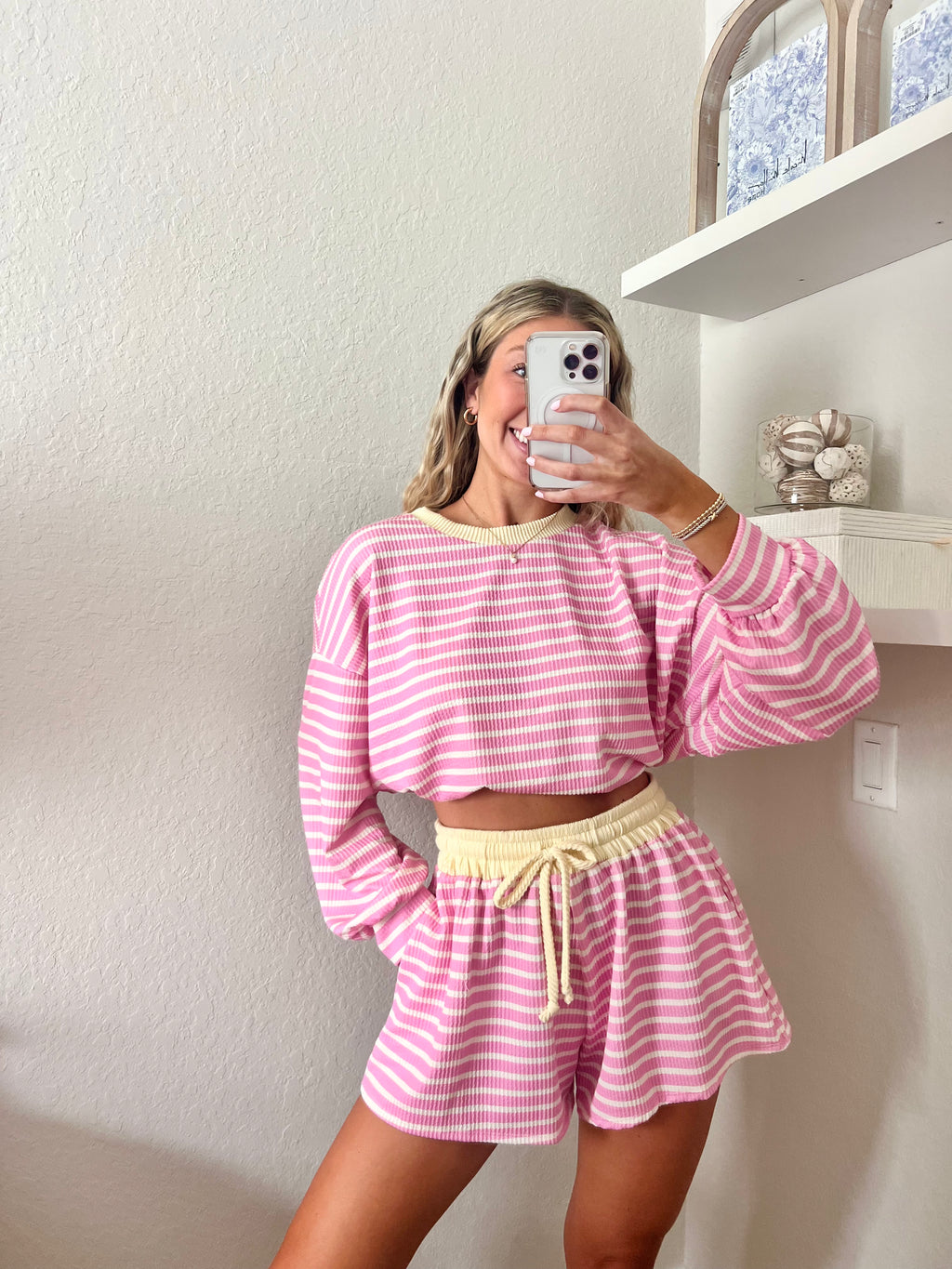 Woman wearing a pink and white striped long sleeve and shorts set with yellow trim taking a mirror selfie.