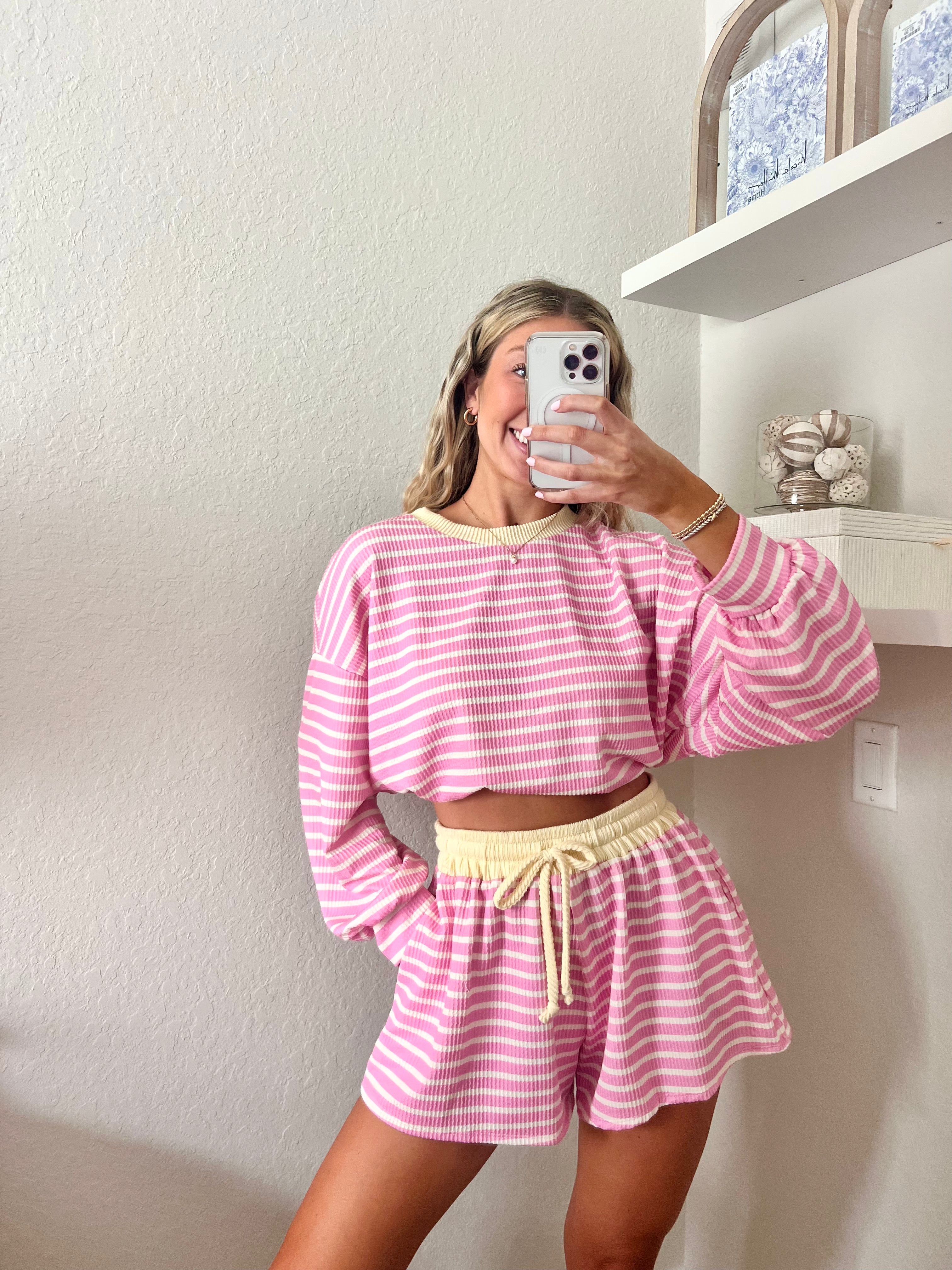 Woman wearing a pink and white striped long sleeve and shorts set with yellow trim taking a mirror selfie.