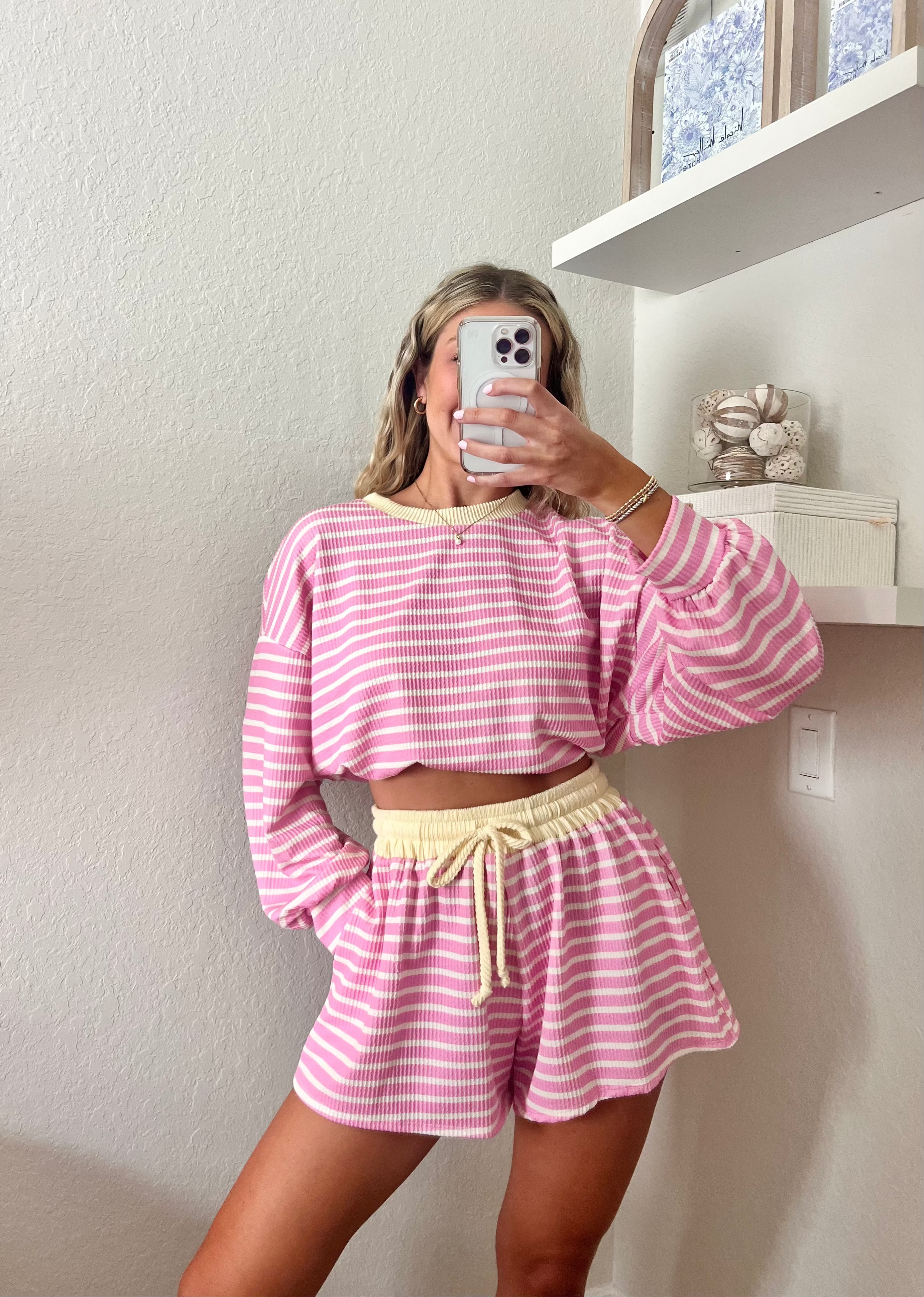 Woman wearing a pink and white striped long sleeve and shorts set with yellow trim taking a mirror selfie.