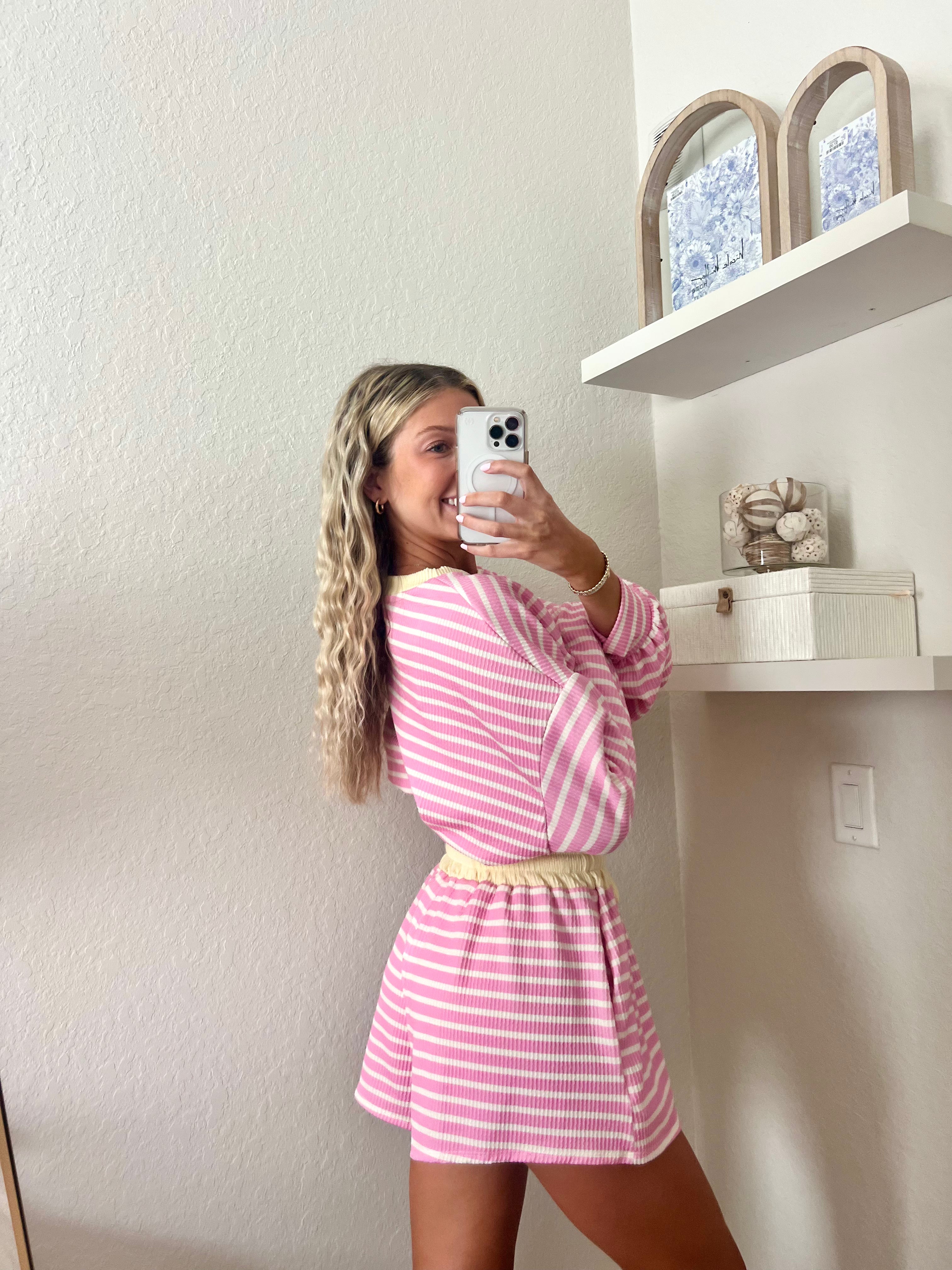 Woman wearing a pink and white striped long sleeve and shorts set with yellow trim taking a mirror selfie.