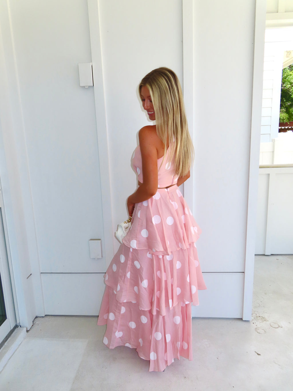 Woman wearing a pink polka dot skirt set holding a white clutch on a bright white patio.