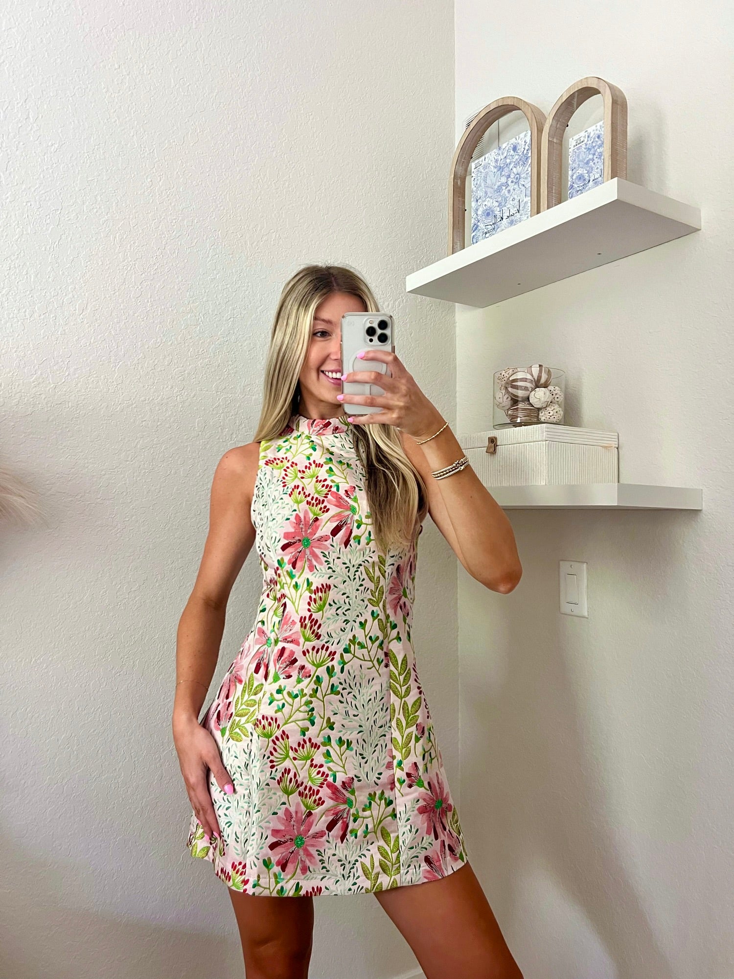 Woman taking a mirror selfie wearing a floral high neck mini dress in a minimalistic room.