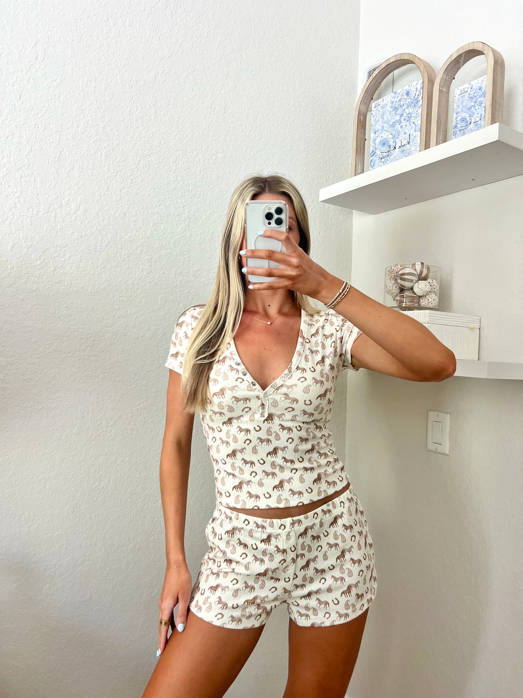 Woman taking a mirror selfie wearing an ivory lounge set with western graphics on it in a room.
