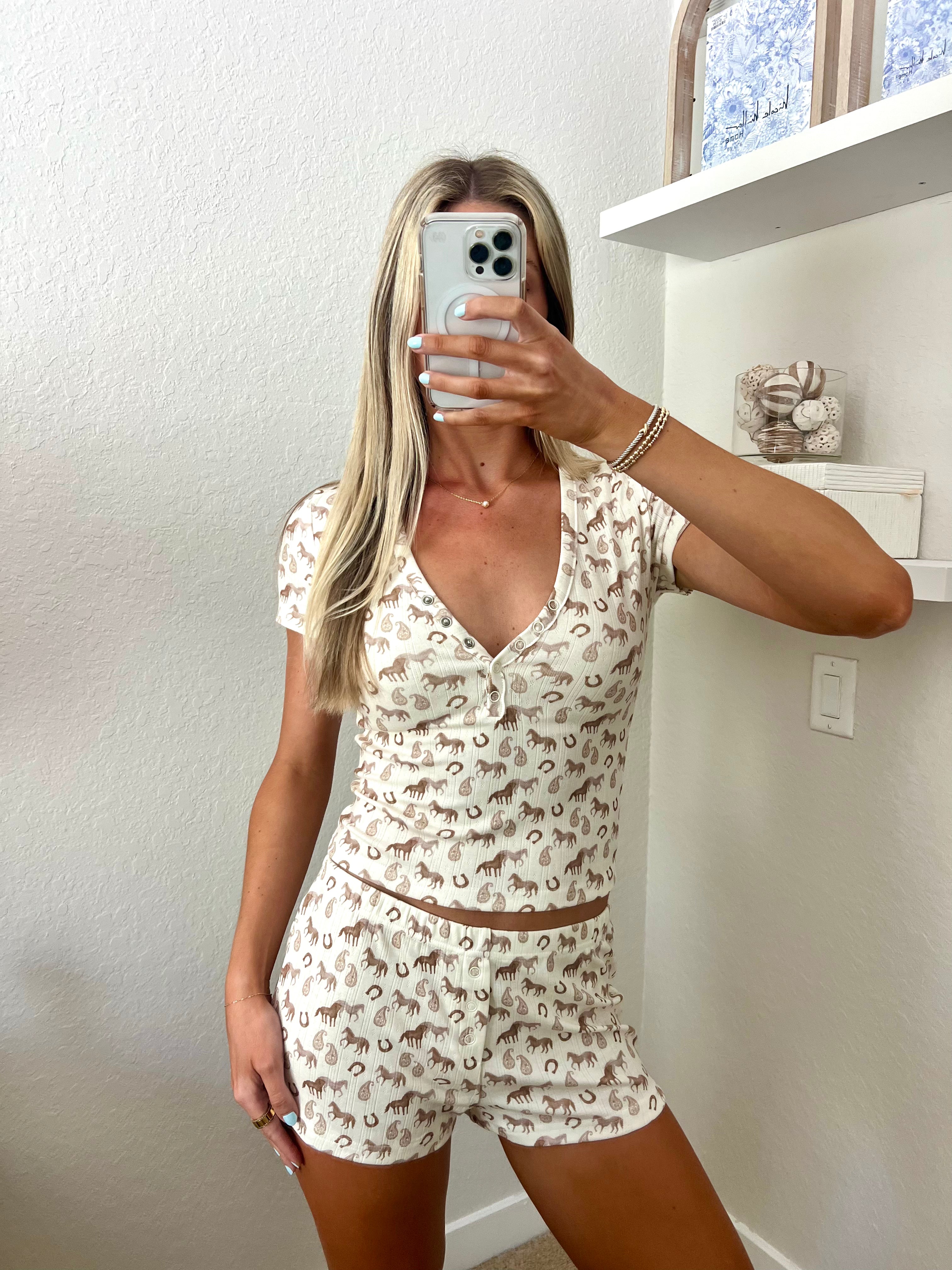 Woman taking a mirror selfie wearing an ivory lounge set with western graphics on it in a room.