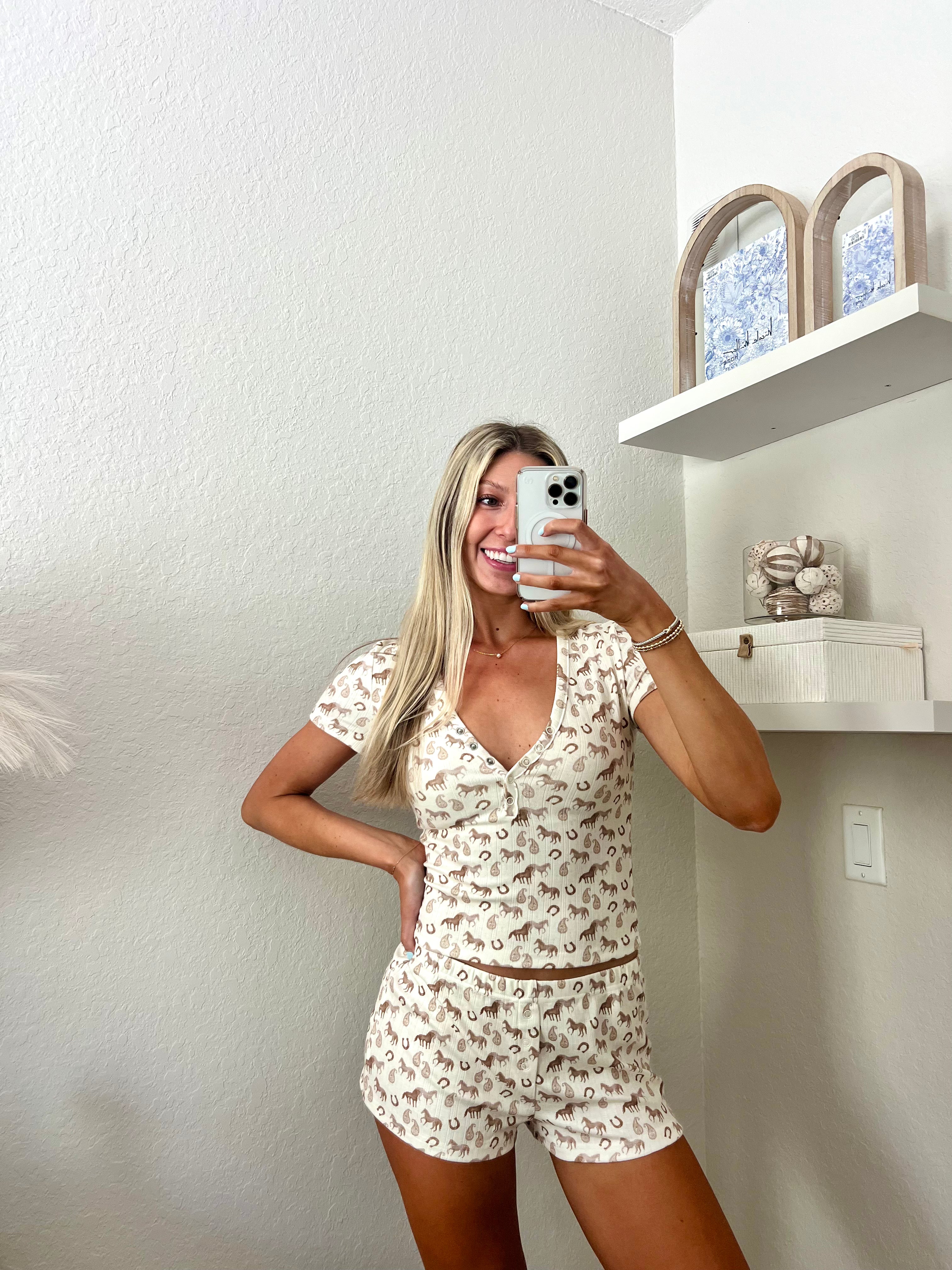 Woman taking a mirror selfie wearing an ivory lounge set with western graphics on it in a room.