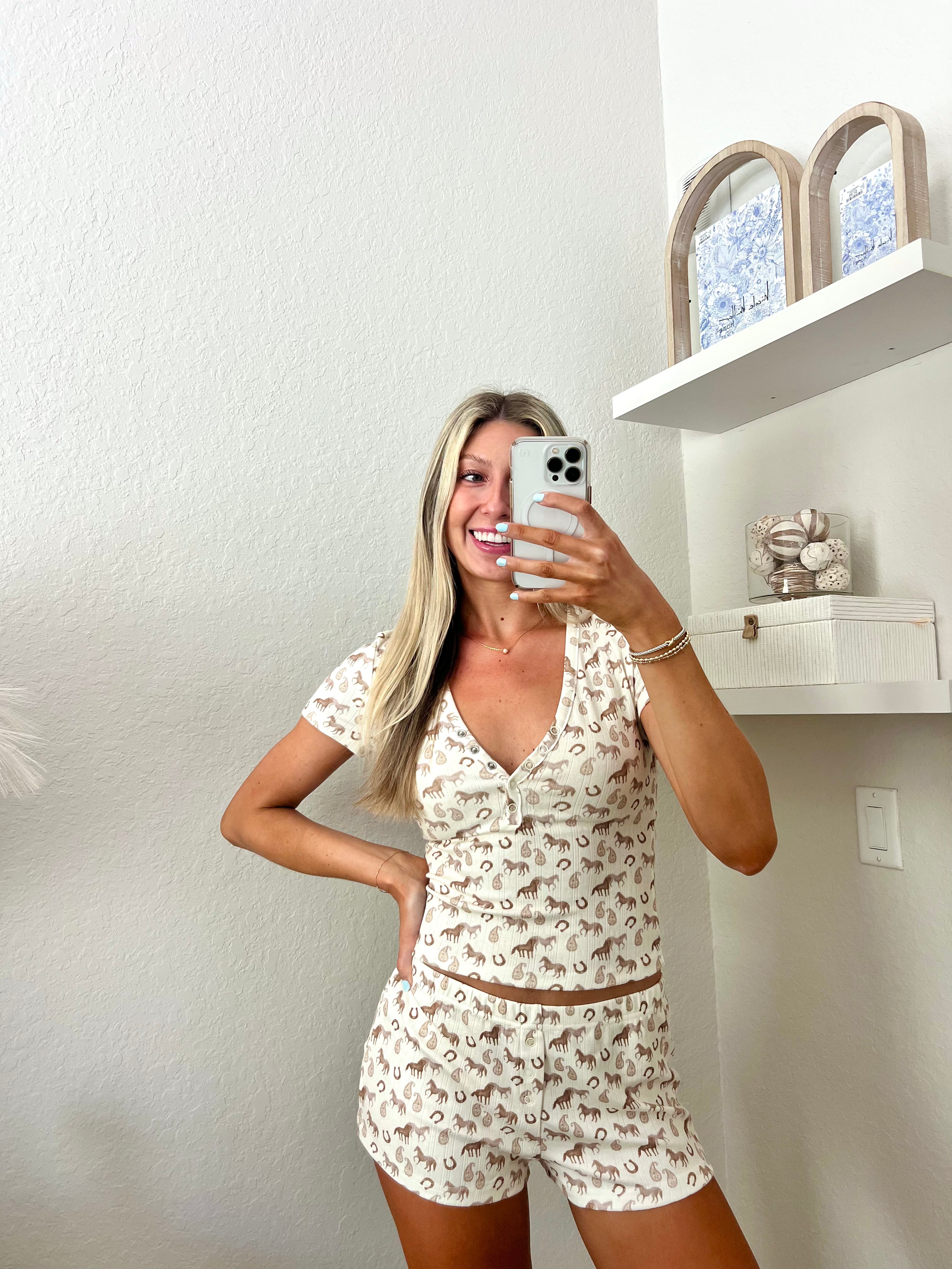 Woman taking a mirror selfie wearing an ivory lounge set with western graphics on it in a room.