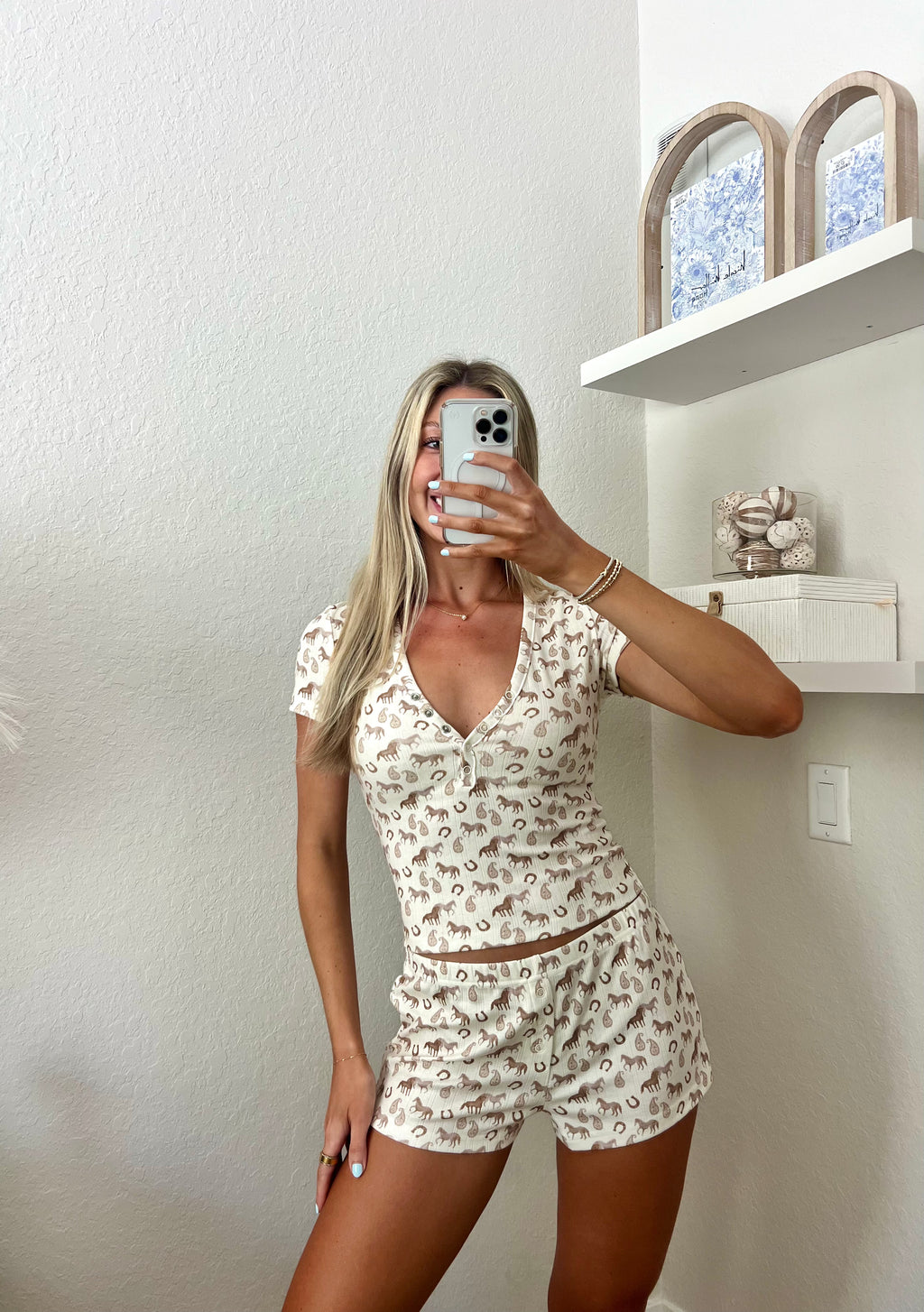 Woman taking a mirror selfie wearing an ivory lounge set with western graphics on it in a room.