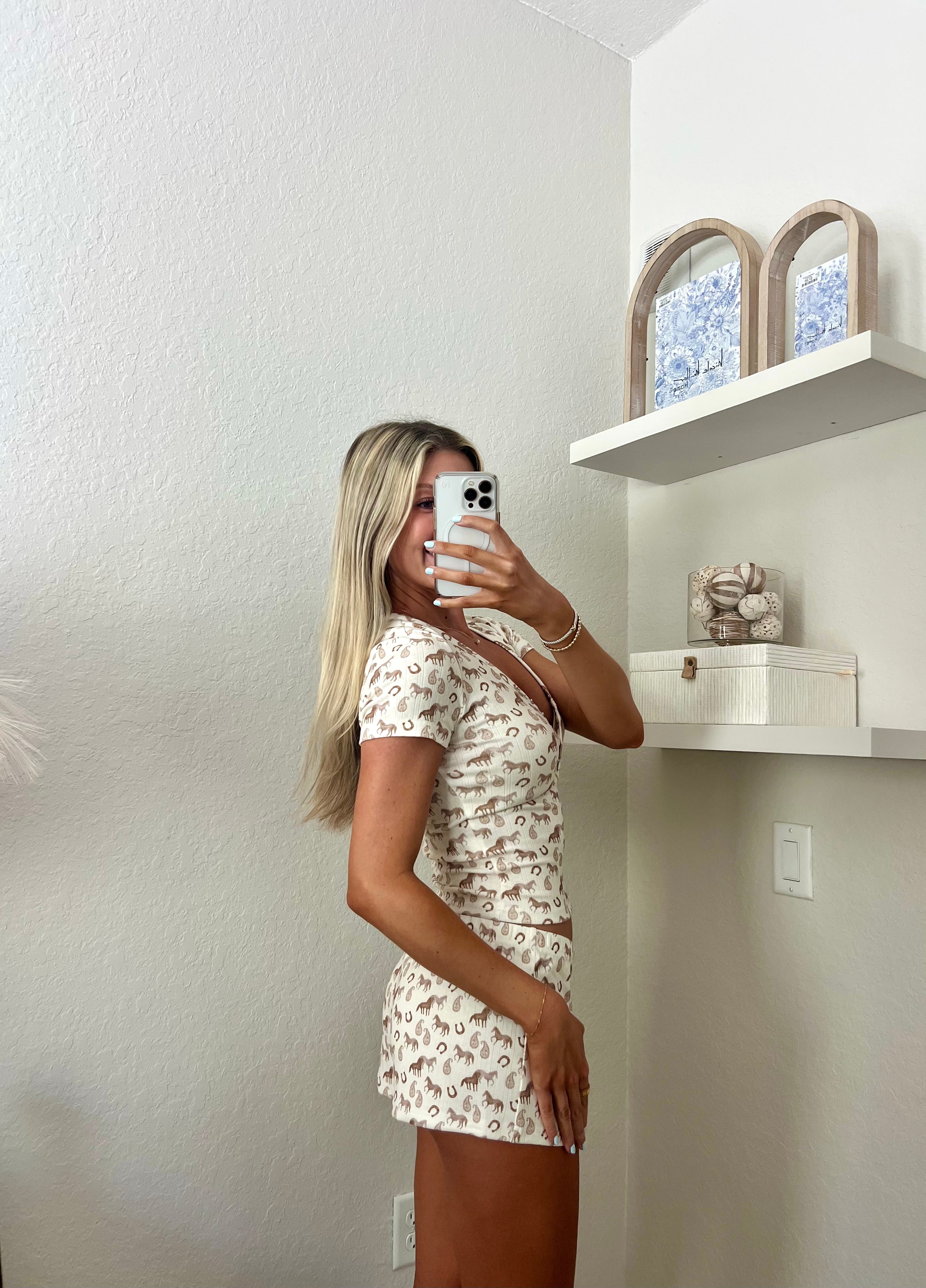Woman taking a mirror selfie wearing an ivory lounge set with western graphics on it in a room.