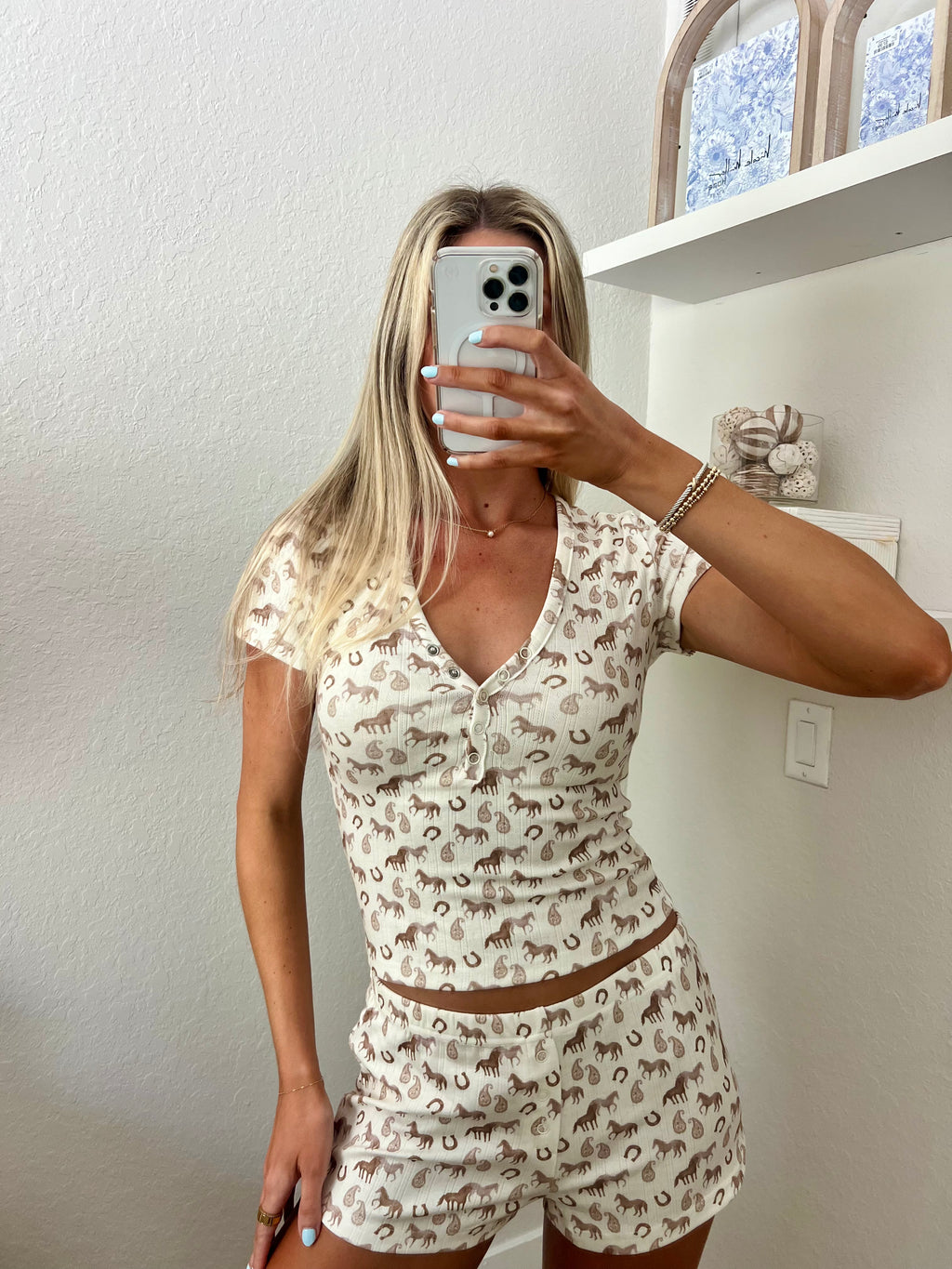 Woman taking a mirror selfie wearing an ivory lounge set with western graphics on it in a room.