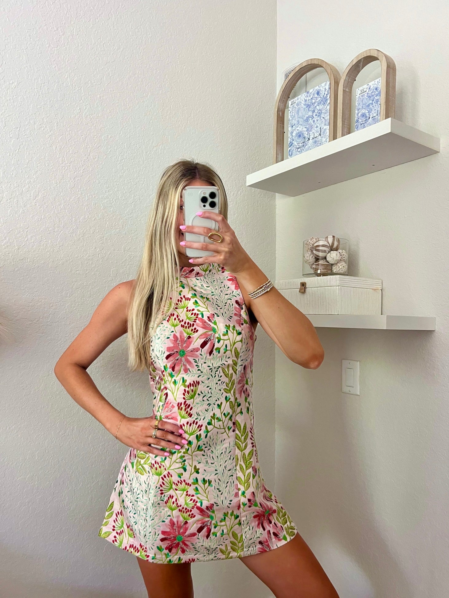 Woman taking a mirror selfie wearing a floral high neck mini dress in a minimalistic room.