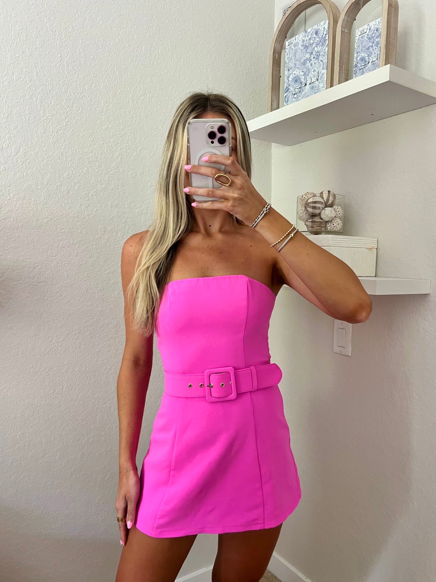 Woman taking a mirror selfie wearing a bright pink strapless dress with a belt.