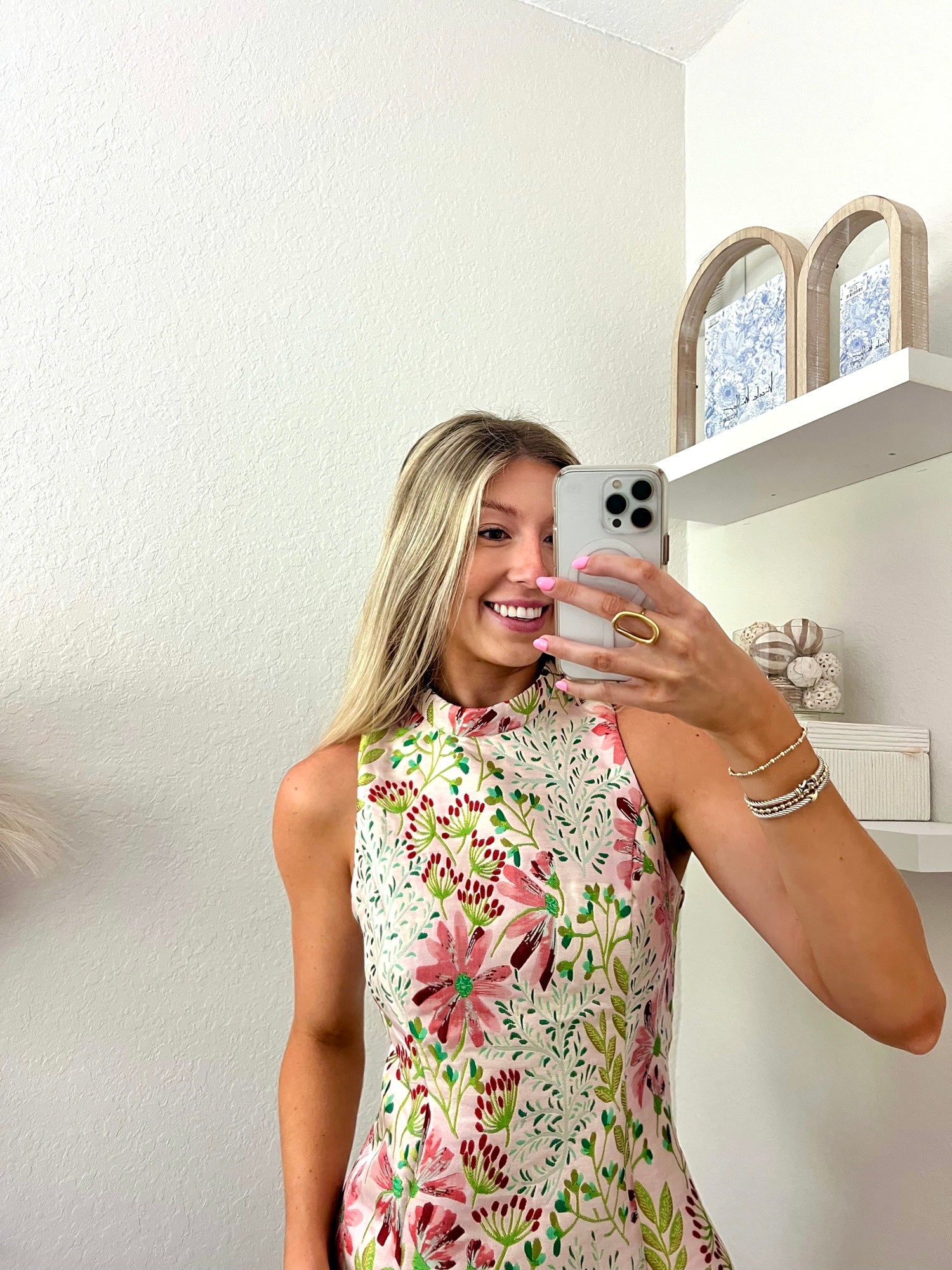 Woman taking a mirror selfie wearing a floral high neck mini dress in a minimalistic room.
