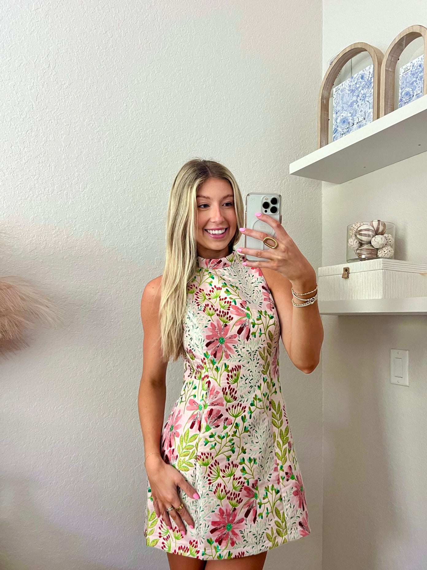 Woman taking a mirror selfie wearing a floral high neck mini dress in a minimalistic room.