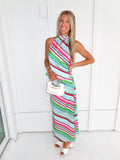 Woman wearing a colorful striped maxi skirt set holding a white handbag and standing in front of a white wall.
