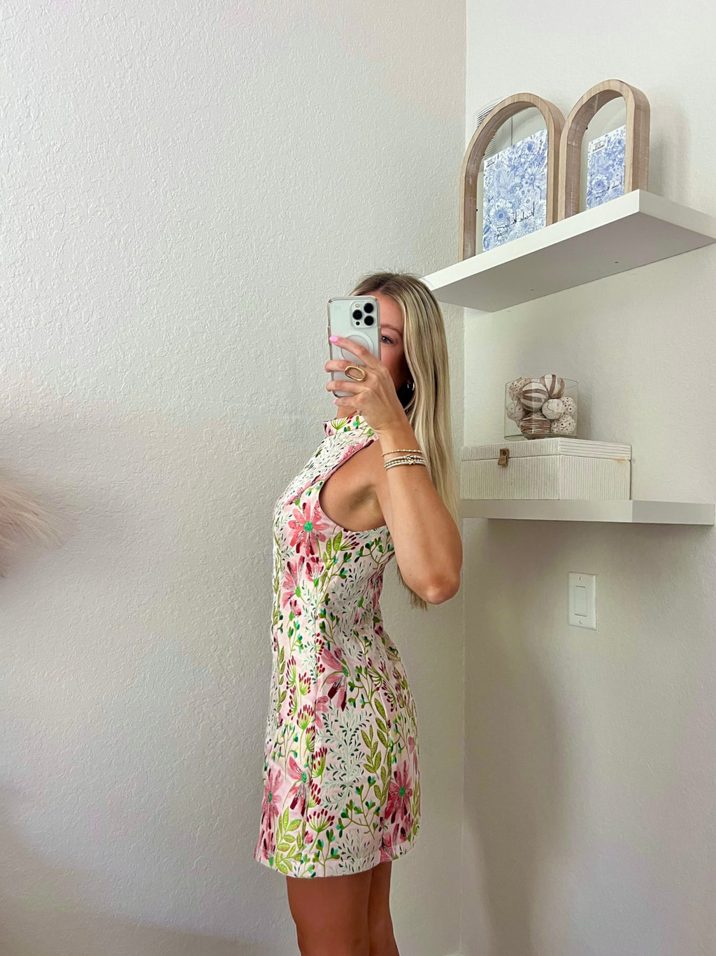 Woman taking a mirror selfie wearing a floral high neck mini dress in a minimalistic room.