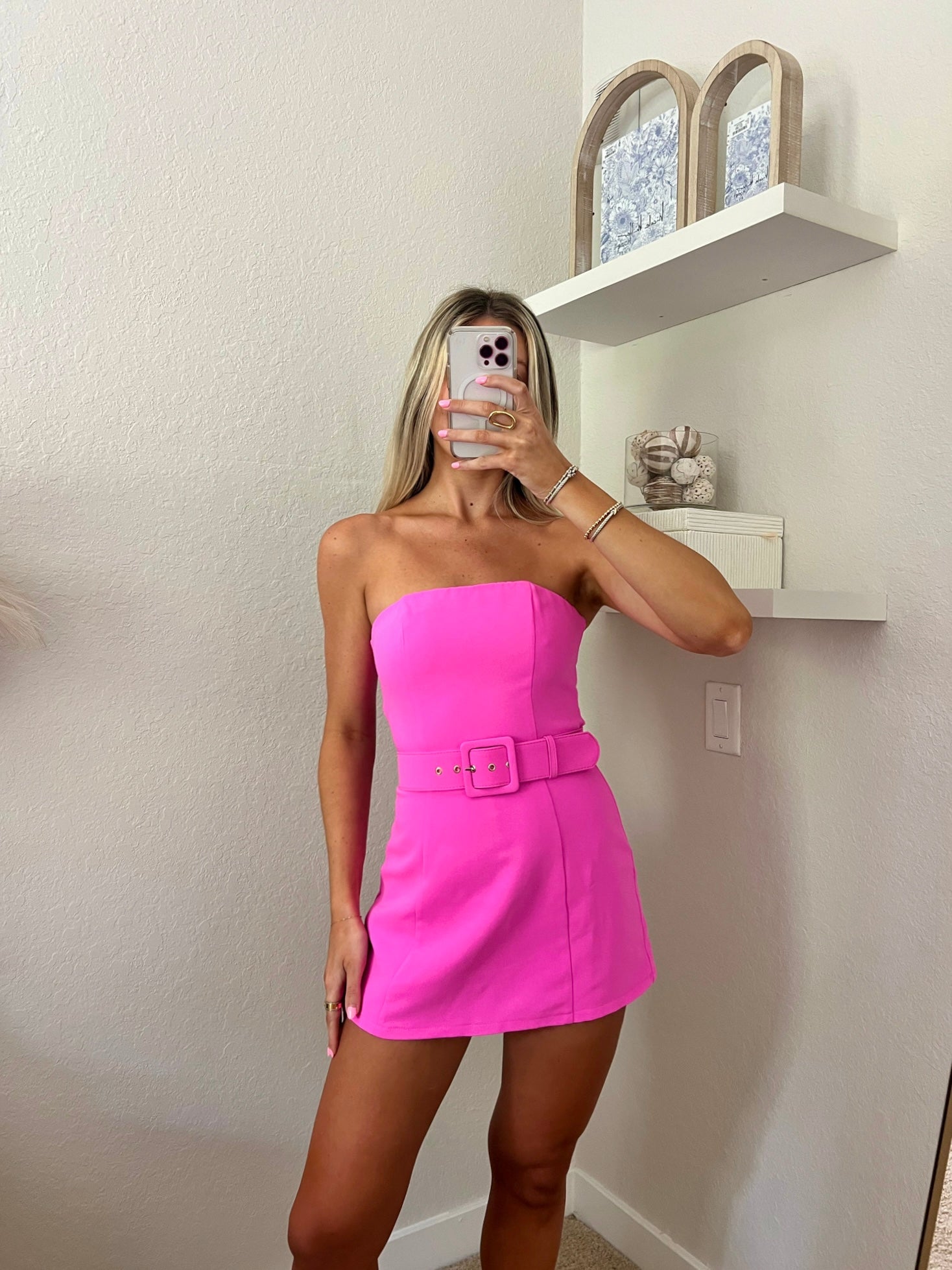 Woman taking a mirror selfie wearing a bright pink strapless dress with a belt.