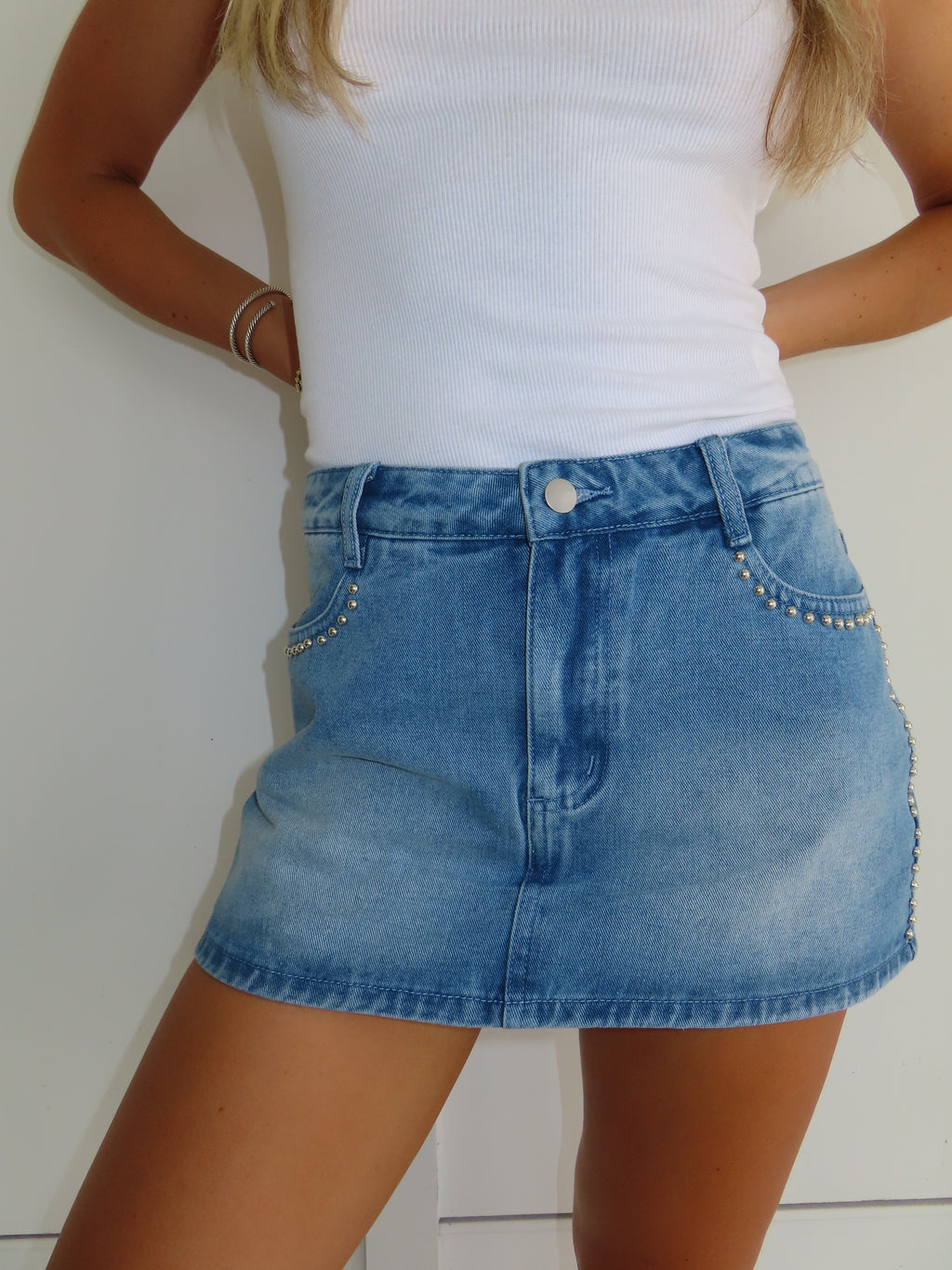Person wearing a blue denim skirt with decorative studs and a white top on a plain background