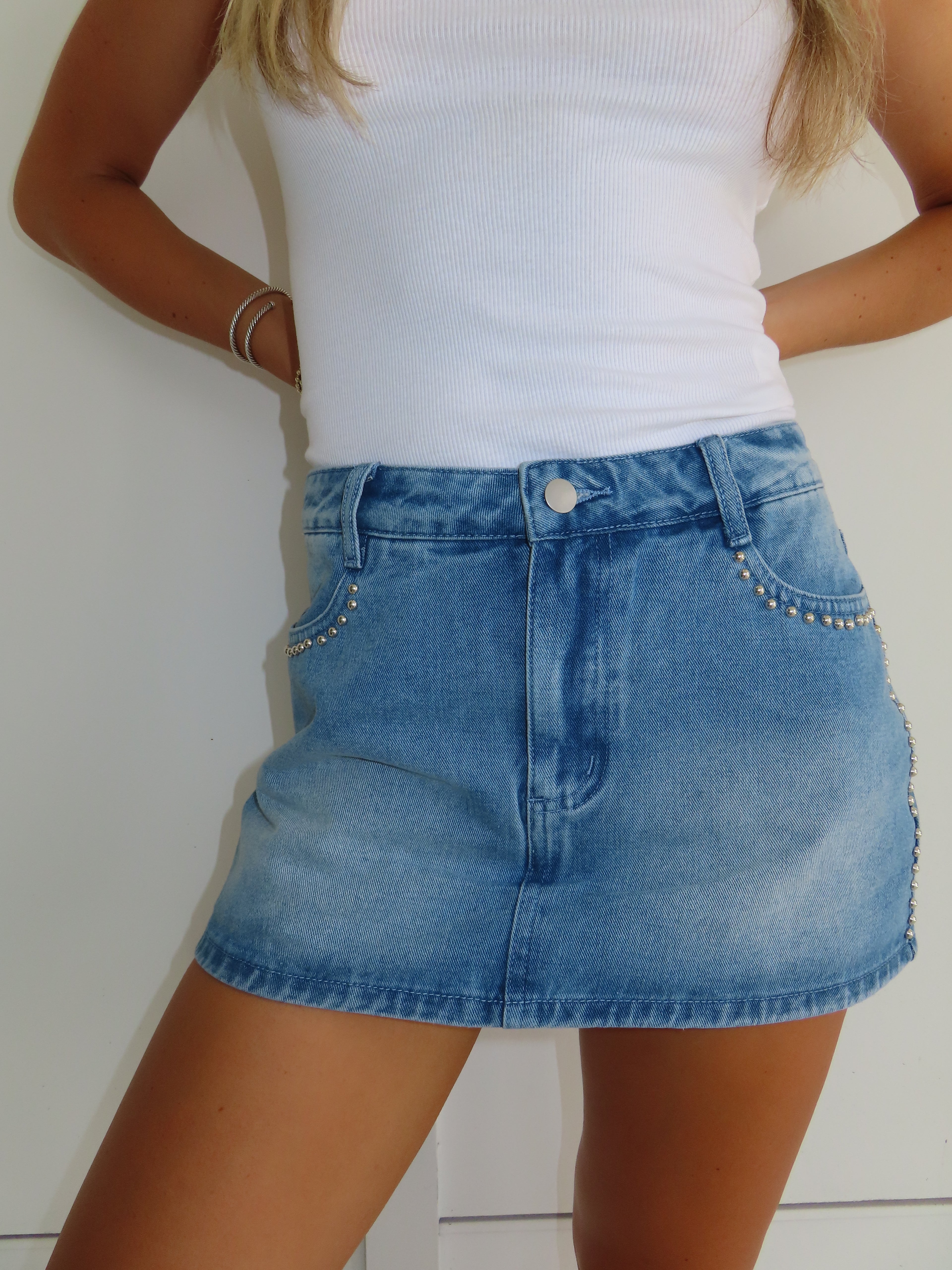 Person wearing a blue denim skirt with decorative studs and a white top on a plain background