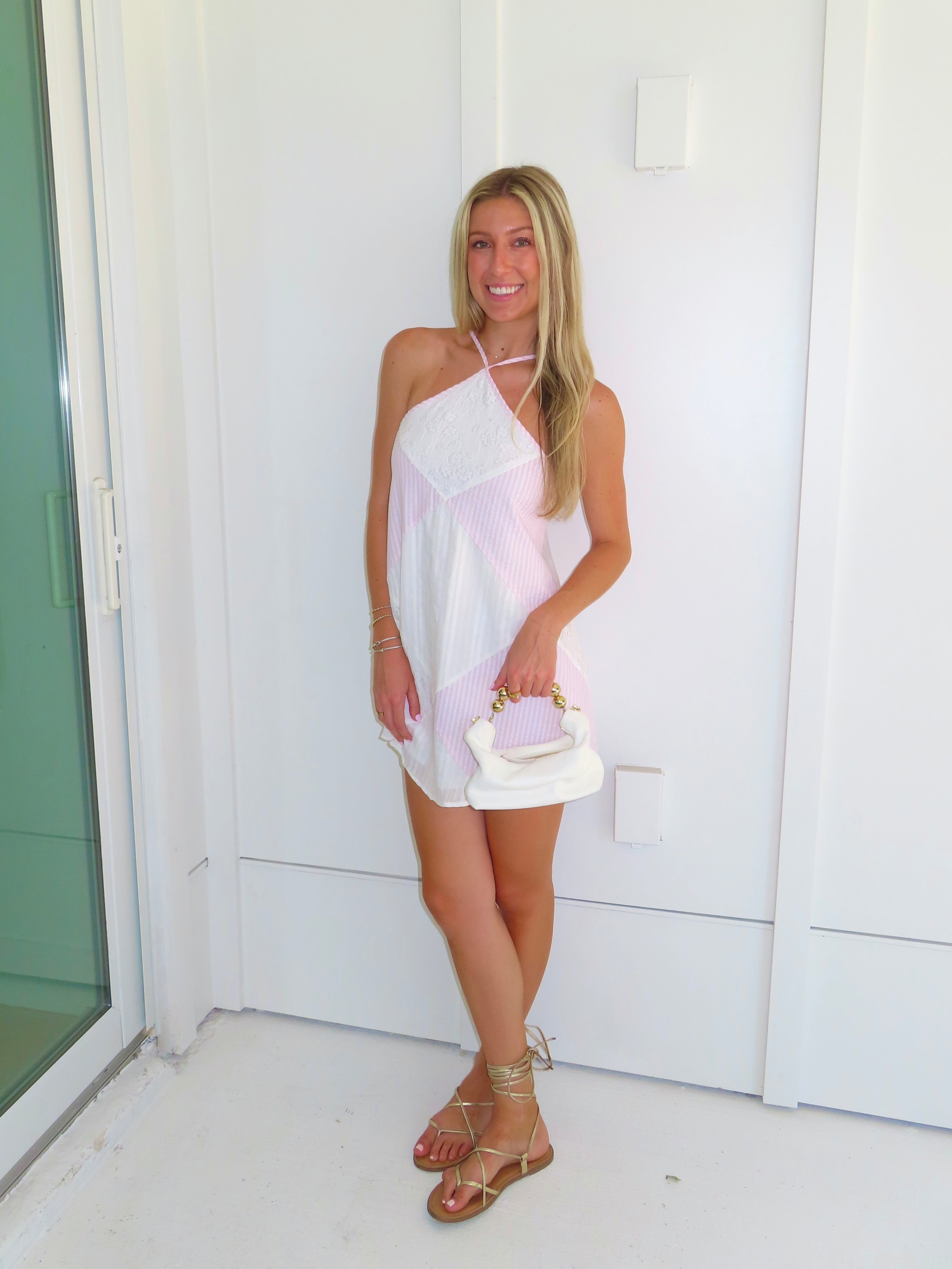 Woman in a white and pink dress holding a clutch against a white background.
