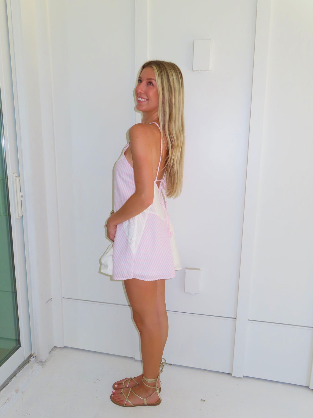 Woman in a white and pink dress holding a clutch against a white background.