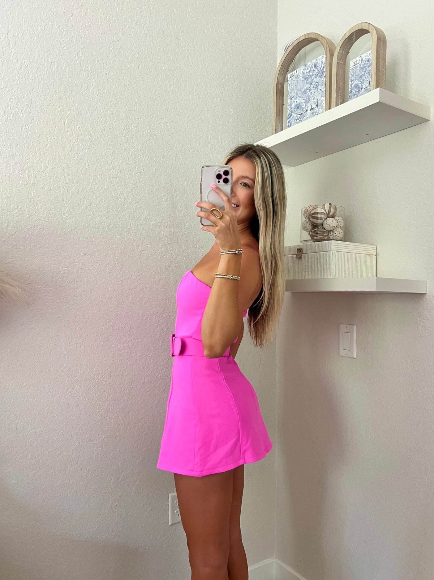 Woman taking a mirror selfie wearing a bright pink strapless dress with a belt.
