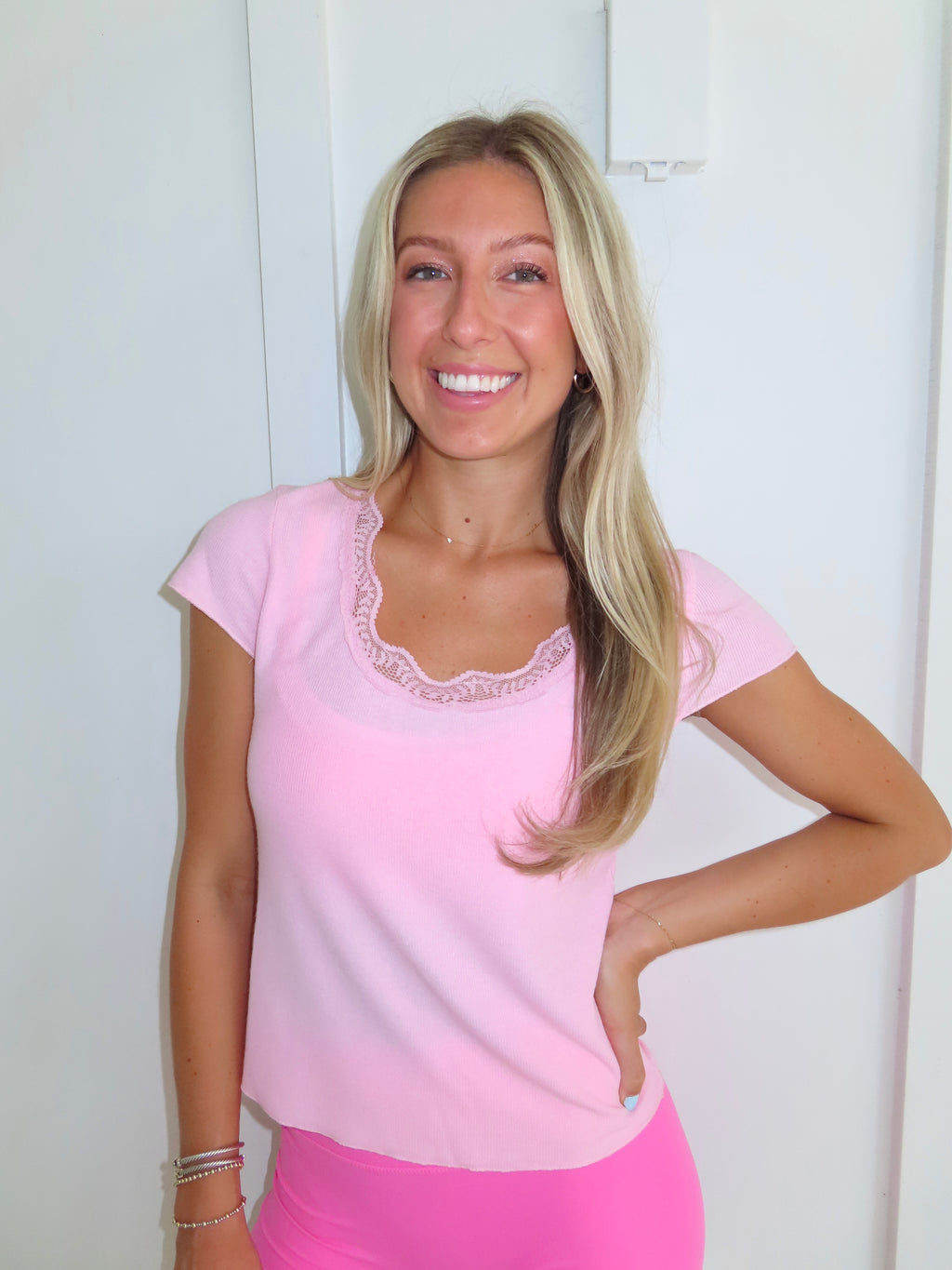 Woman wearing a pink tee and pink bikers shorts with pink sneakers standing against a white wall.