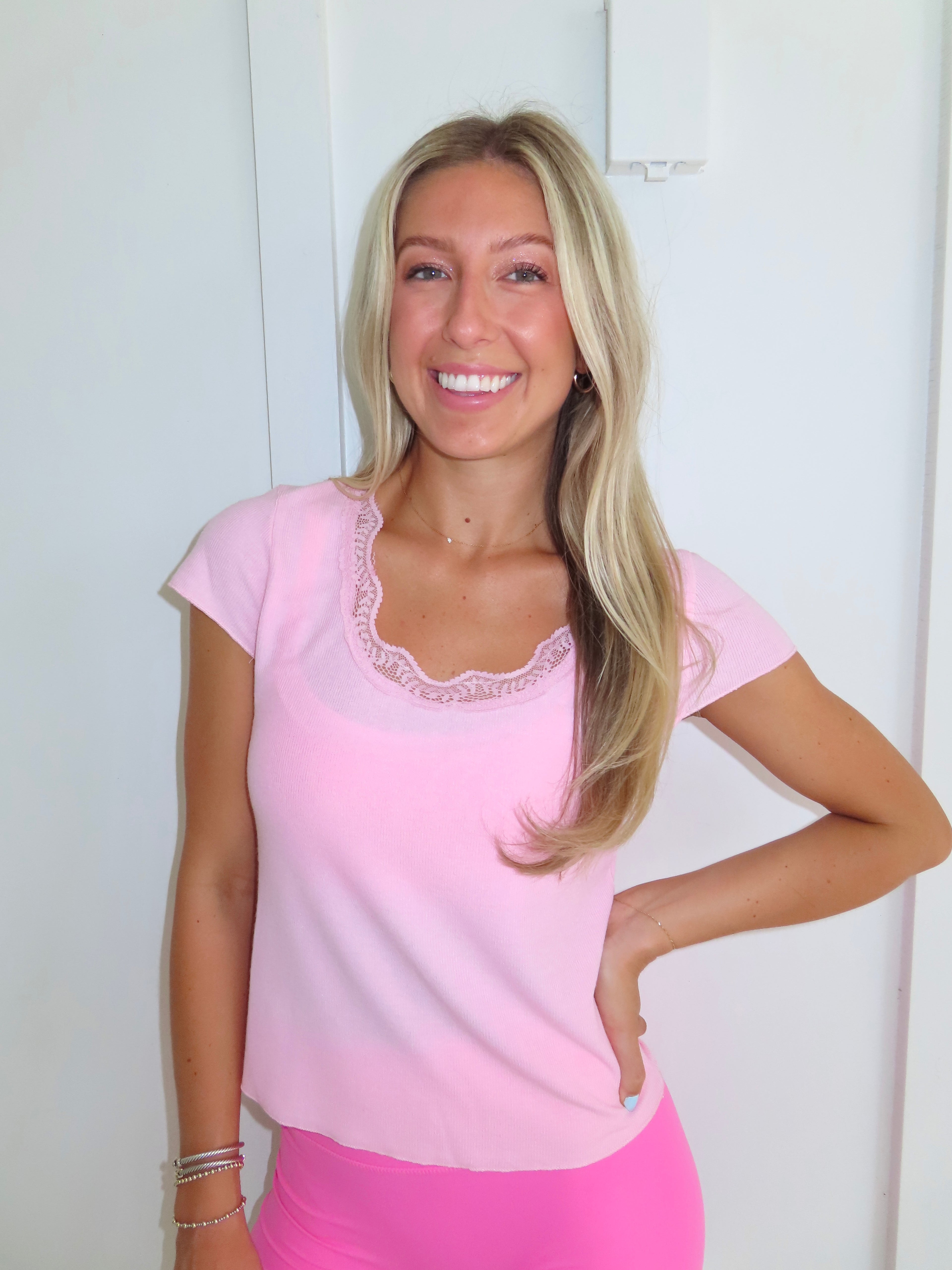 Woman wearing a pink tee and pink bikers shorts with pink sneakers standing against a white wall.