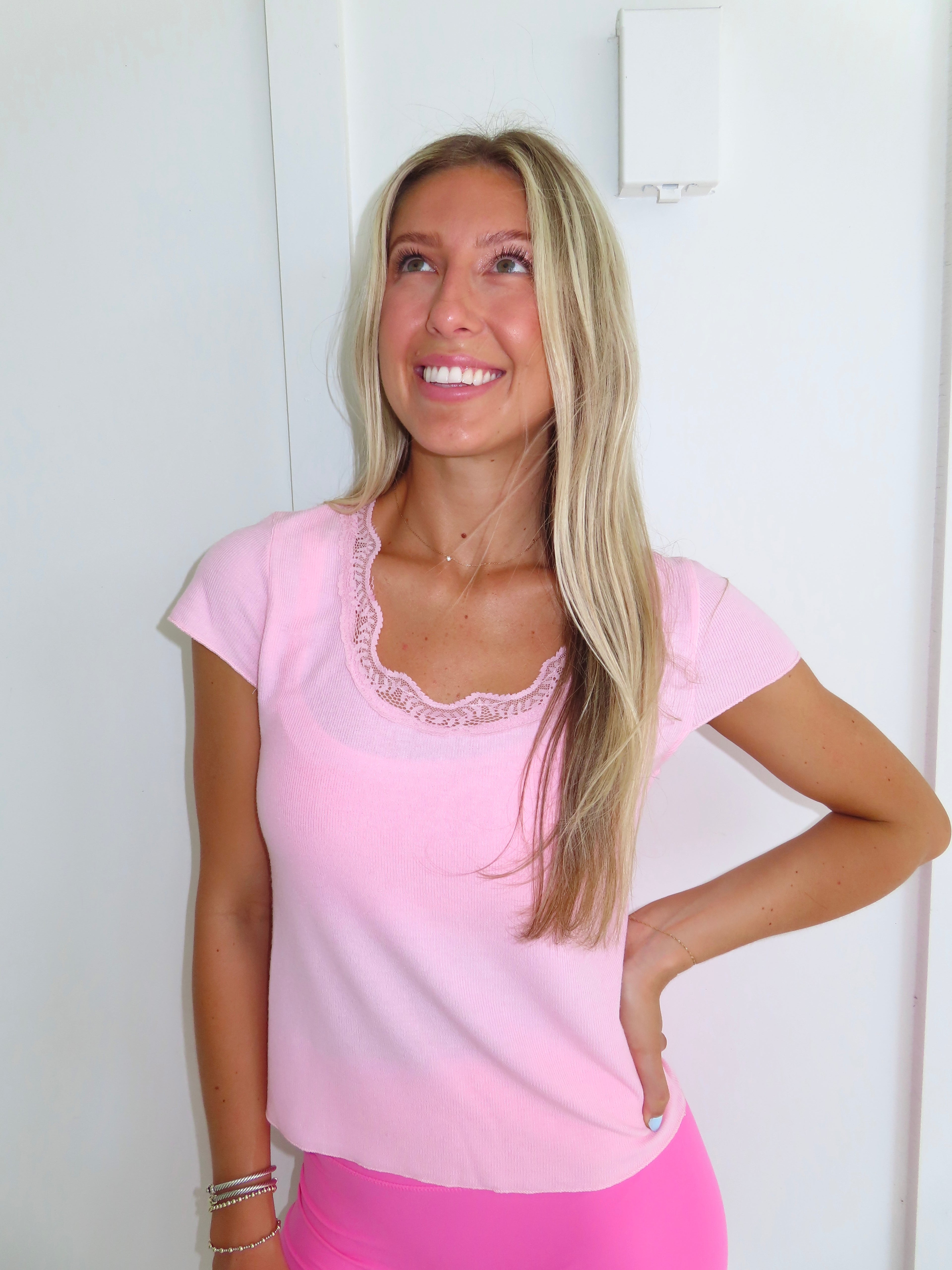 Woman wearing a pink tee and pink bikers shorts with pink sneakers standing against a white wall.