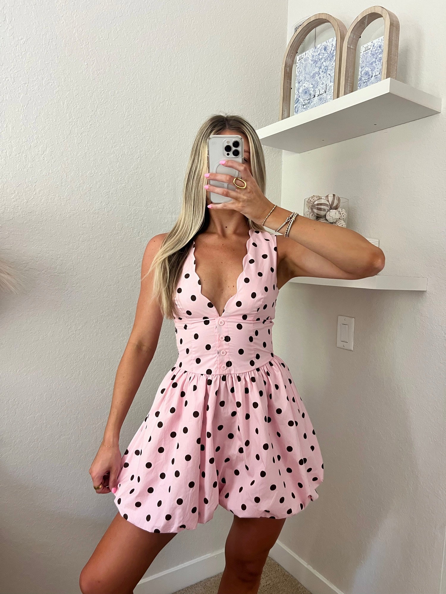 Woman taking a mirror selfie wearing a pink mini dress with brown polka.