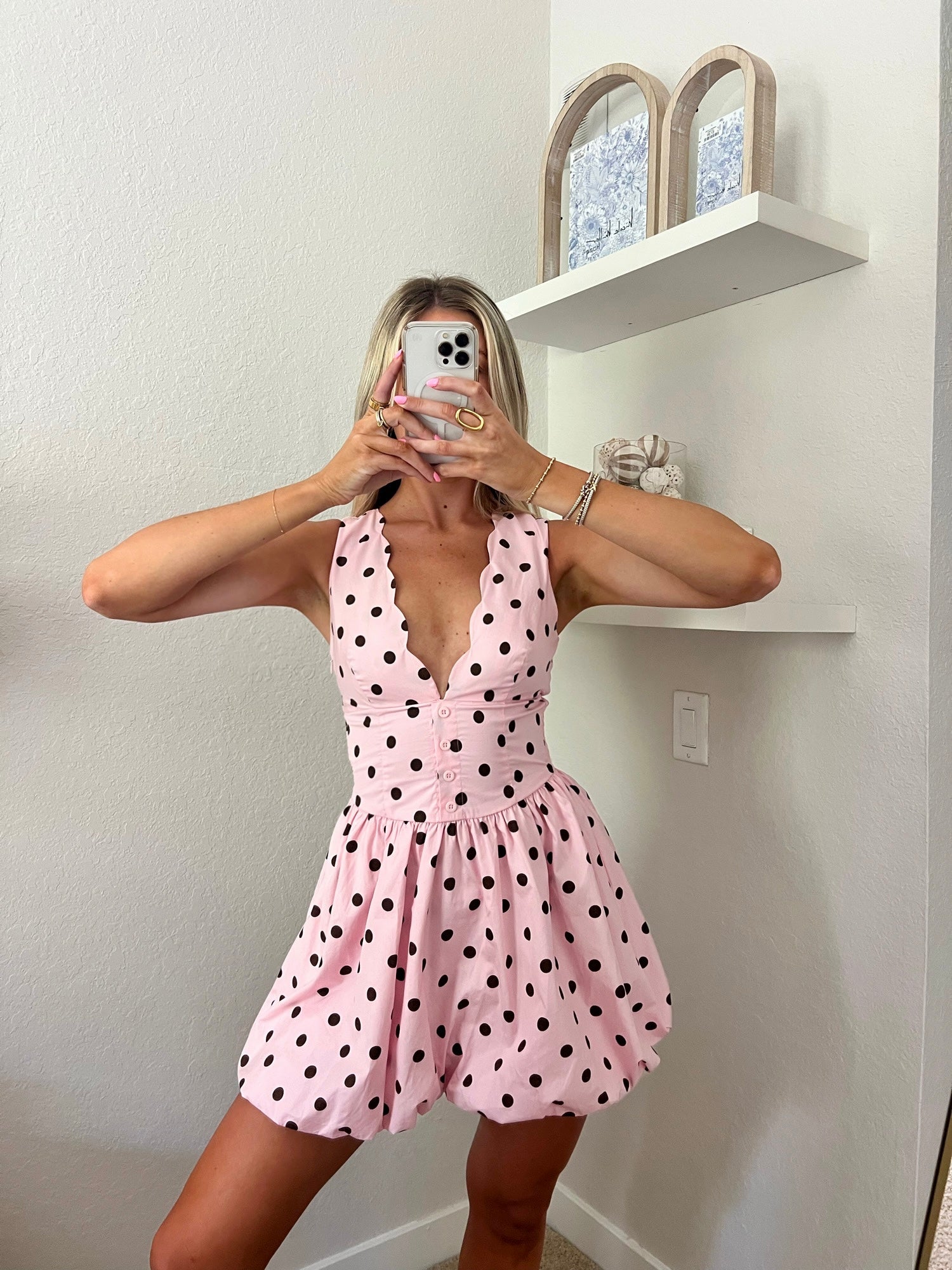Woman taking a mirror selfie wearing a pink mini dress with brown polka.