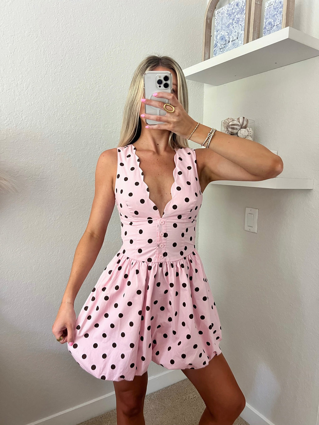 Woman taking a mirror selfie wearing a pink mini dress with brown polka.