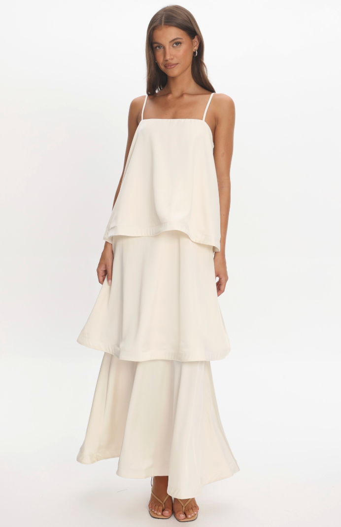 A woman modeling a cream-colored tiered  layered maxi dress standing against a white background.