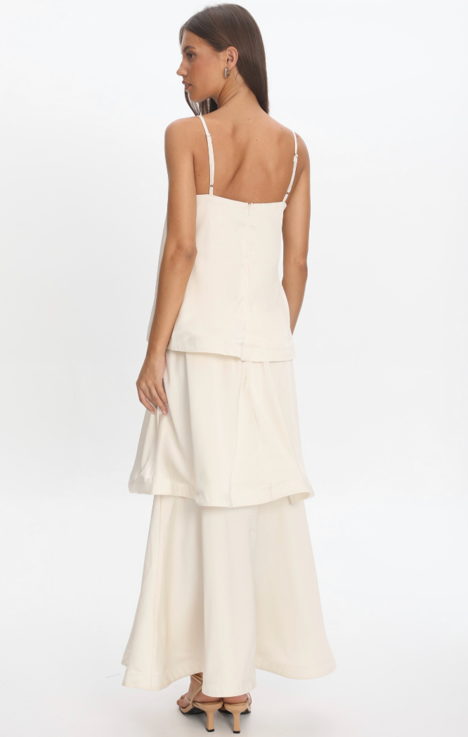 A woman modeling a cream-colored tiered  layered maxi dress standing against a white background.